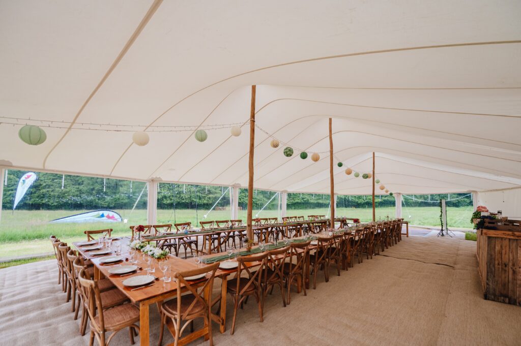 white marquee / stretch tent with walls by countryside events, with rustic furniture, wooden bar and rustic king poles with lanterns strung between