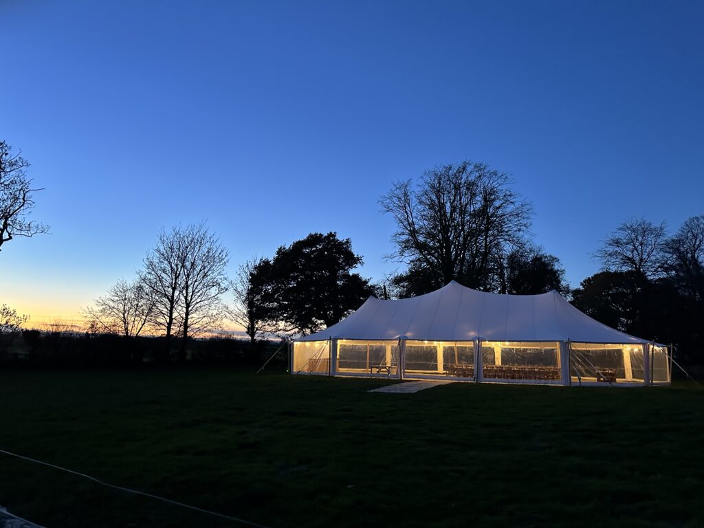 'Penhill' 12x26m White Stretch Marquee at night with sun setting behind trees