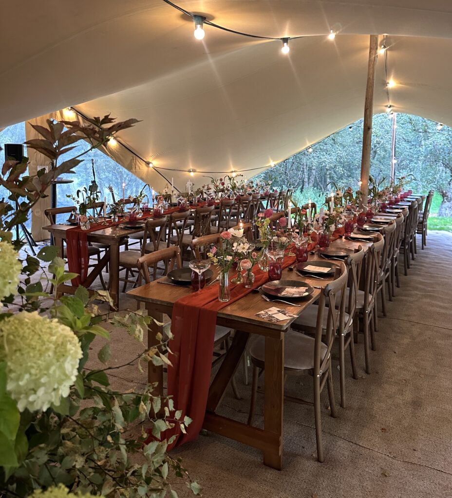 stretch tent with autumnal dining scheme, festoon lights, long rustic dining tables and seasonal flowers