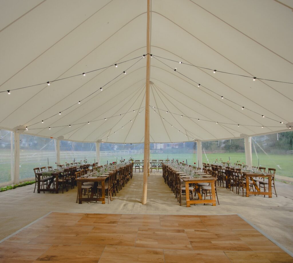 white marquee interior with long rustic tables, wooden dance floor and festoon lights