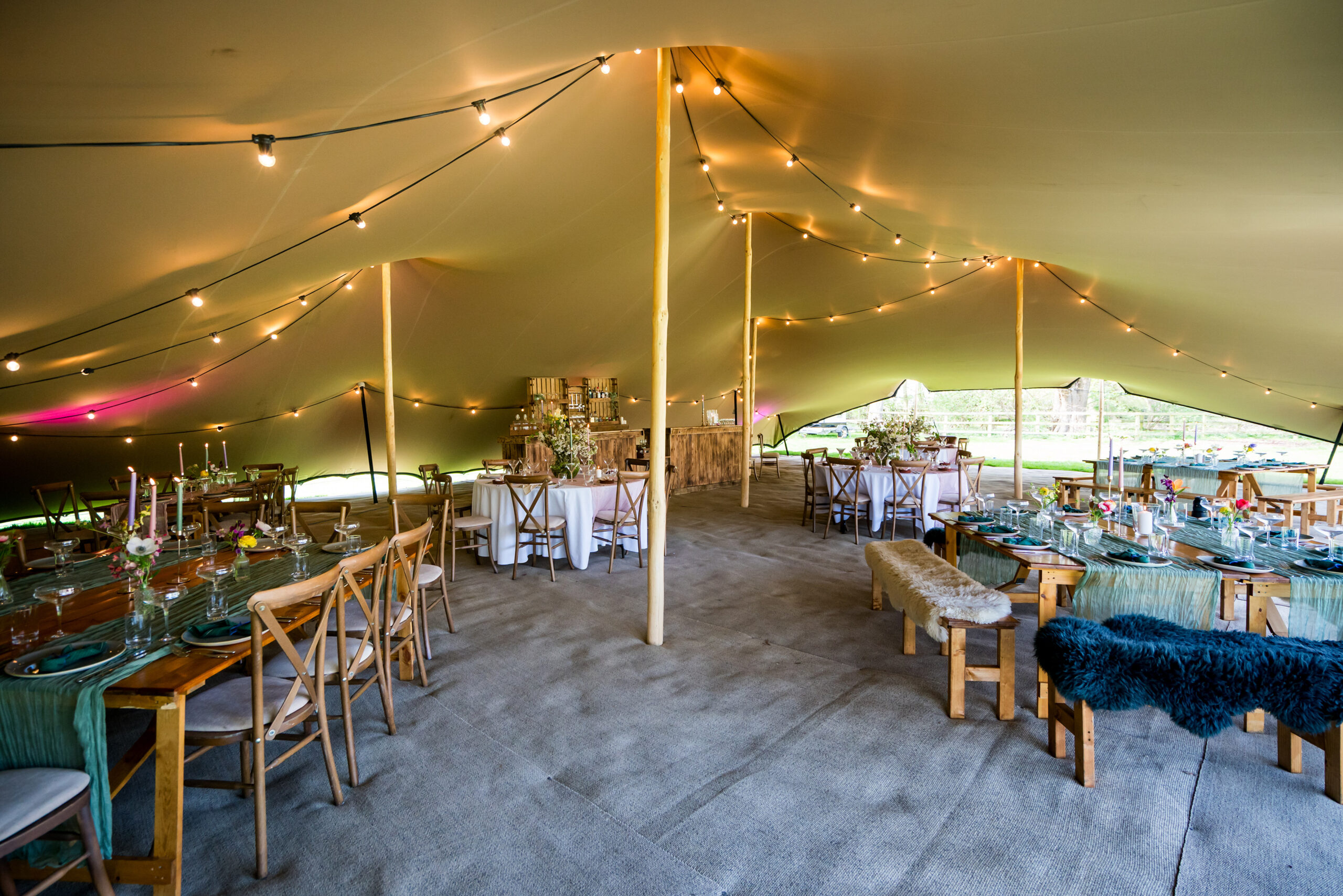 large stretch tent with festoon lighting, rustic furniture and spring flowers