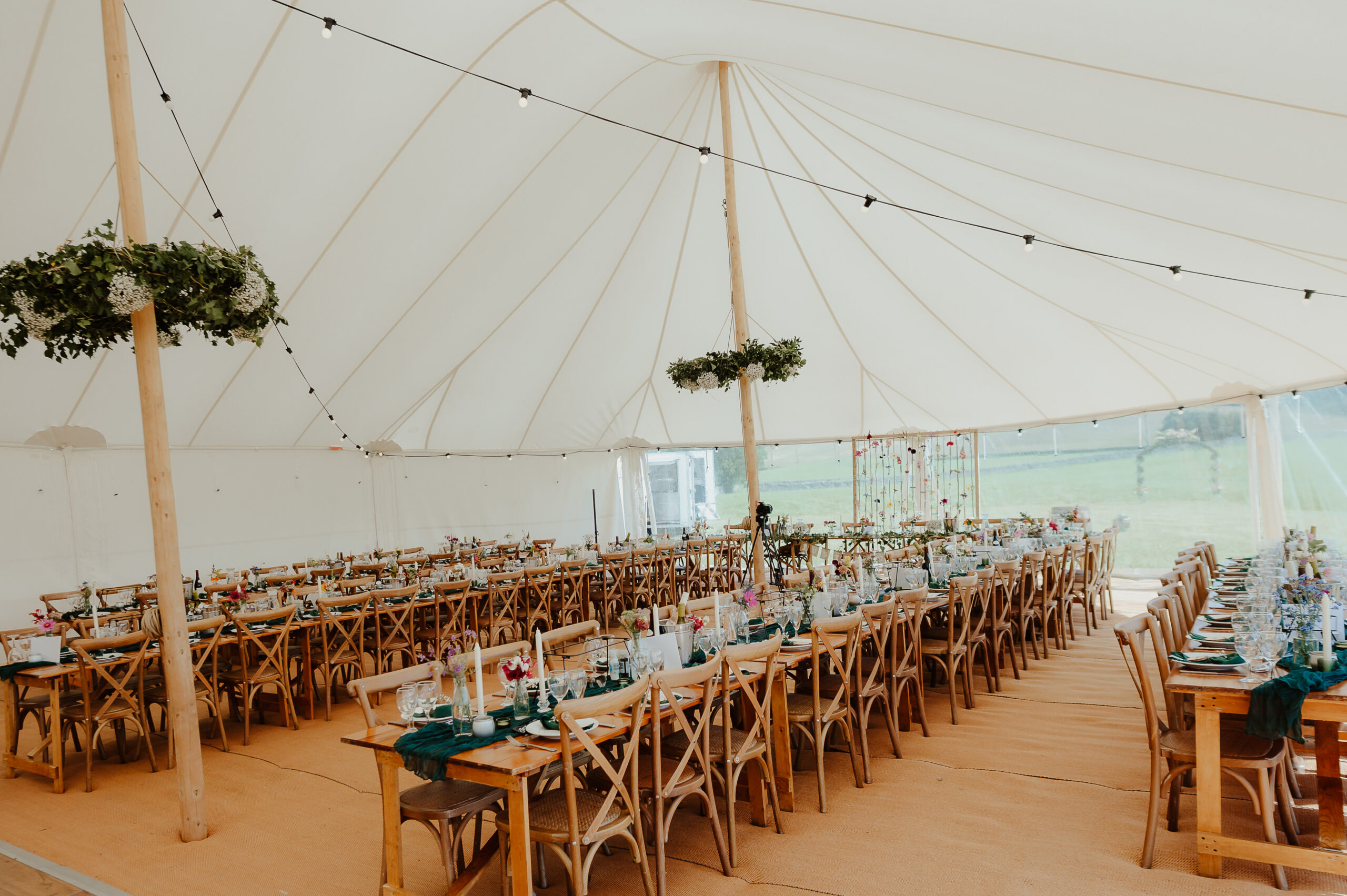 rustic long dining tables in a white wedding marquee, with solid walls to back and clear walls to front, floristry hoops and green table runners decorated with summer flowers, marquee by Countryside Events, photo by Helen Elizabeth Weddings